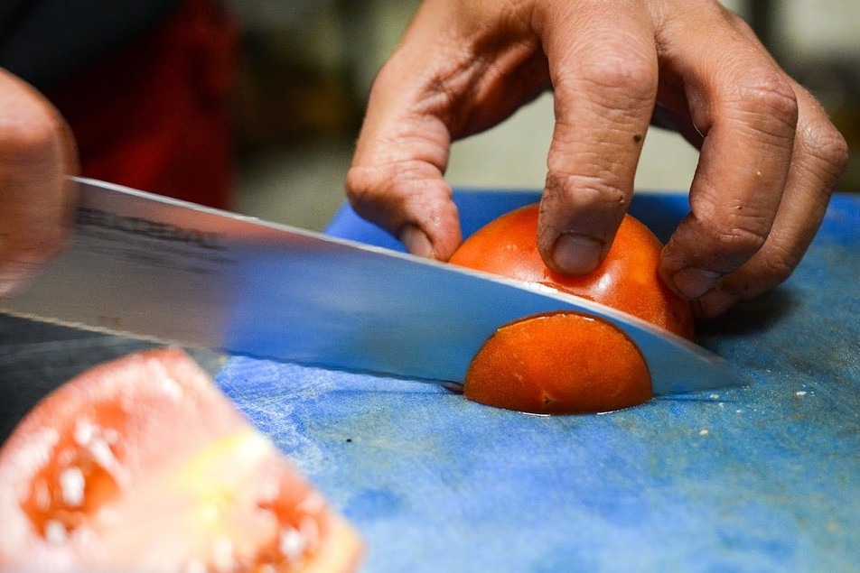 a chef’s hand slicing a tomato with a kitchen knife