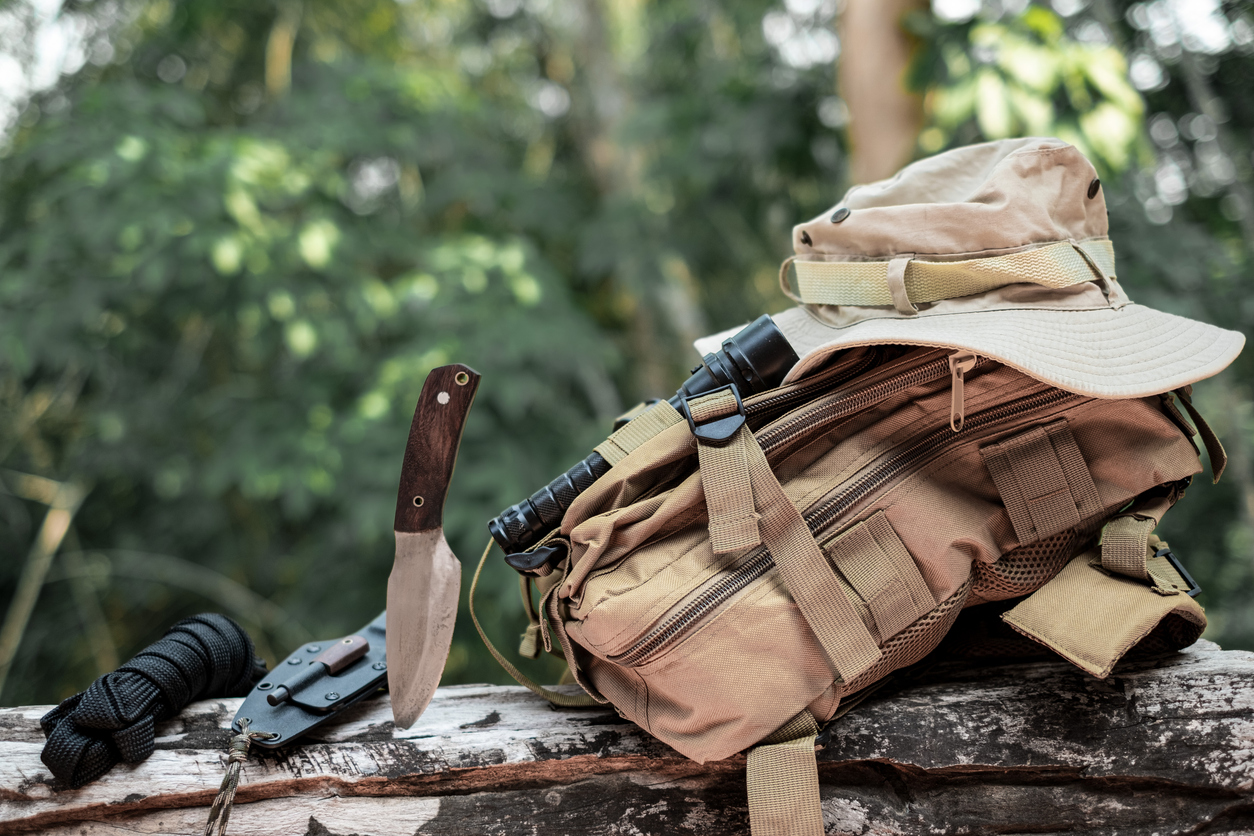 Equipment for survival bucket hat backpack hiking knife camping flashlight resting on wooden timber in the background
