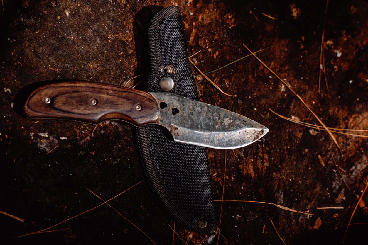 A horizontal, moody flat lay of a fixed-blade knife with a wooden handle lying on its black sheath